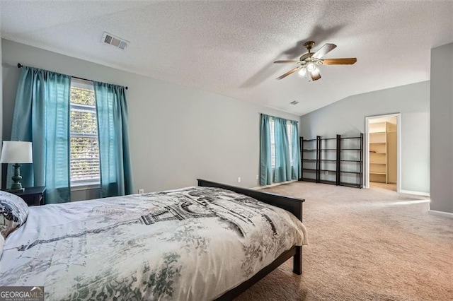 carpeted bedroom featuring a closet, ceiling fan, a textured ceiling, a walk in closet, and lofted ceiling