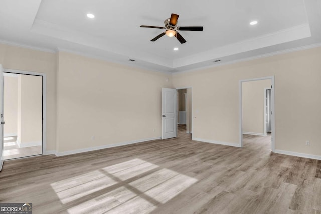 empty room with light hardwood / wood-style floors, ornamental molding, and a tray ceiling