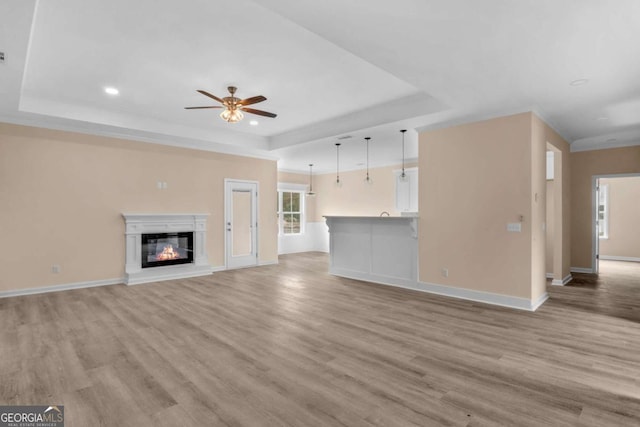 unfurnished living room featuring a raised ceiling, ceiling fan, and light hardwood / wood-style flooring