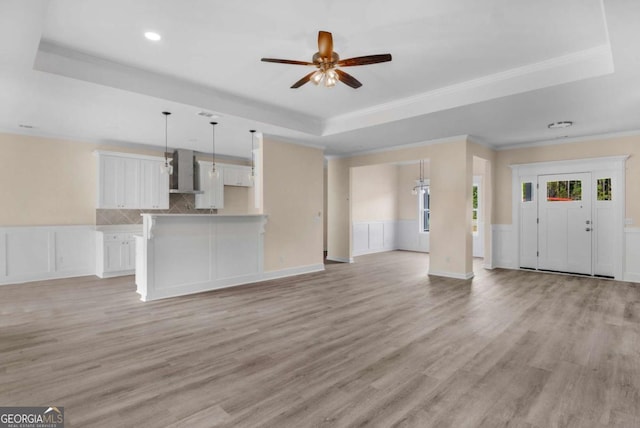 unfurnished living room featuring ceiling fan, light wood-type flooring, a tray ceiling, and ornamental molding