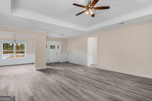 unfurnished living room with ceiling fan, ornamental molding, a raised ceiling, and hardwood / wood-style flooring