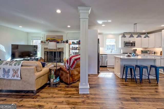 living room featuring ornate columns, a stone fireplace, sink, and dark hardwood / wood-style floors