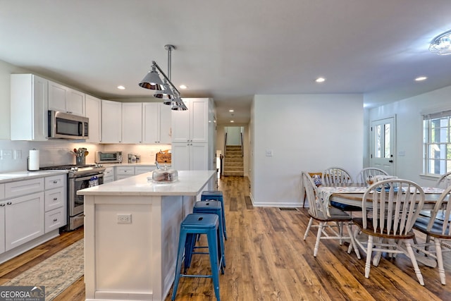 kitchen featuring stainless steel appliances, hanging light fixtures, a kitchen island, white cabinets, and light hardwood / wood-style flooring