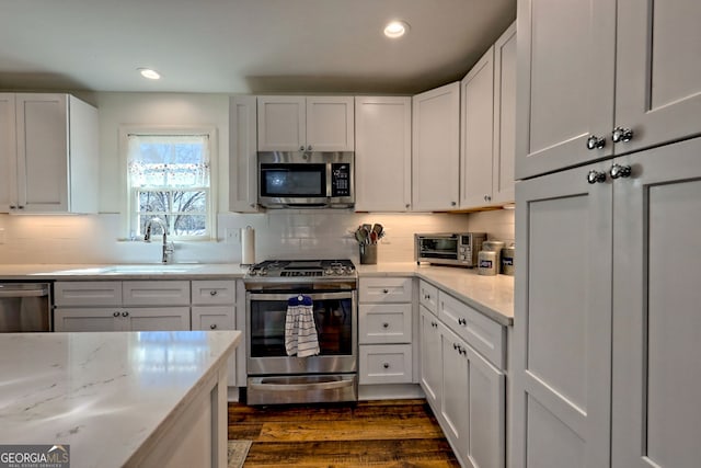 kitchen with appliances with stainless steel finishes, dark hardwood / wood-style floors, white cabinets, and decorative backsplash