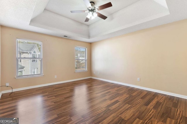 spare room with ceiling fan, dark wood-type flooring, a raised ceiling, and a textured ceiling