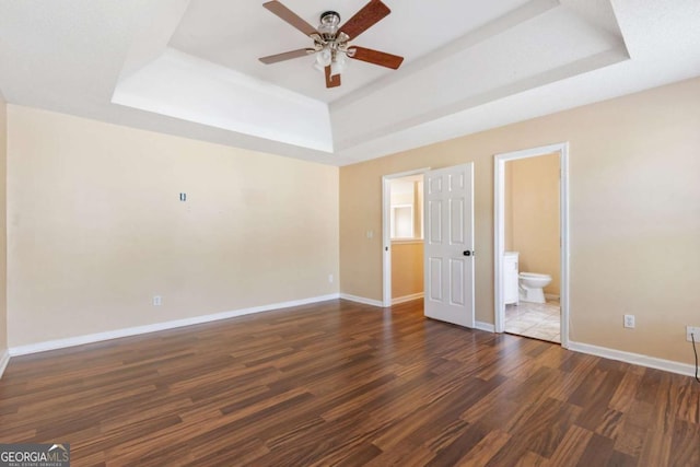 unfurnished bedroom with ceiling fan, dark hardwood / wood-style flooring, connected bathroom, and a tray ceiling