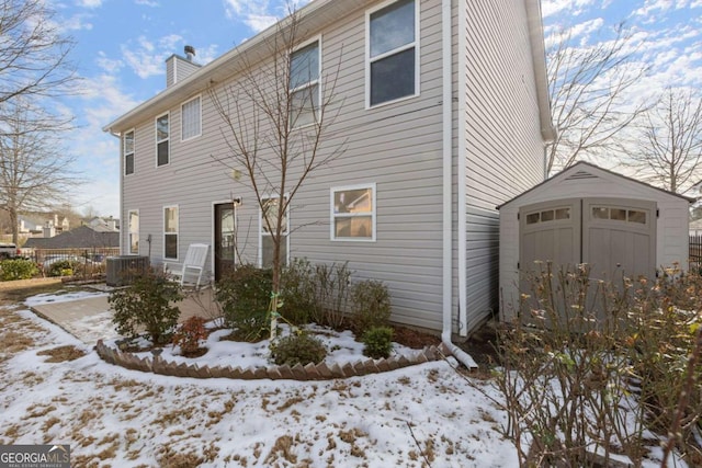 snow covered rear of property with central AC and a storage shed