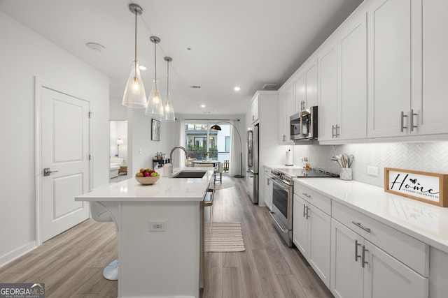 kitchen featuring an island with sink, stainless steel appliances, white cabinets, a breakfast bar, and sink