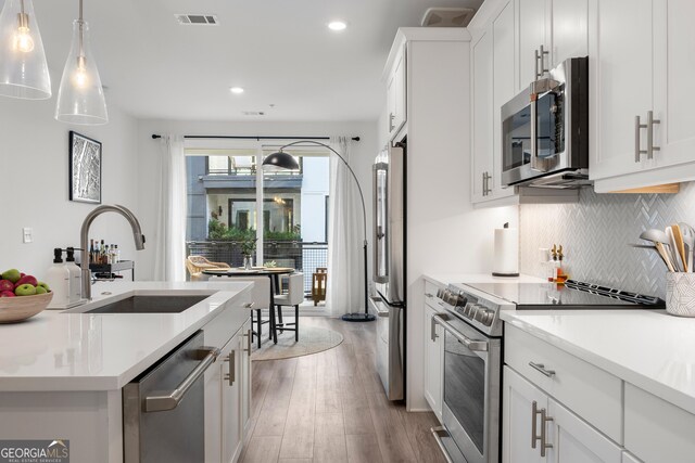 kitchen featuring a center island with sink, a breakfast bar, white cabinetry, hanging light fixtures, and stainless steel appliances