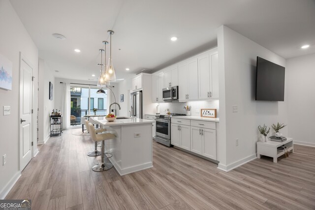 kitchen with white cabinets, appliances with stainless steel finishes, a kitchen breakfast bar, hanging light fixtures, and a kitchen island with sink