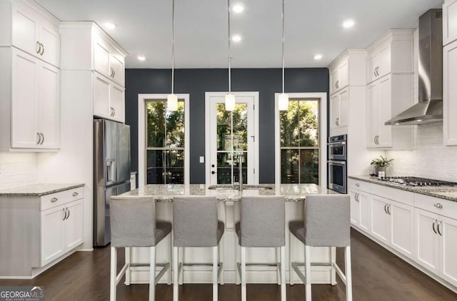 kitchen with pendant lighting, appliances with stainless steel finishes, wall chimney exhaust hood, and white cabinets