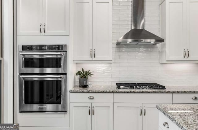 kitchen featuring appliances with stainless steel finishes, wall chimney exhaust hood, and white cabinets