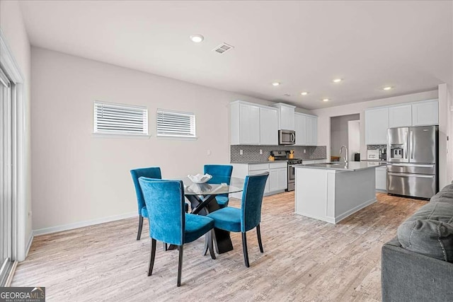 kitchen with appliances with stainless steel finishes, white cabinetry, an island with sink, light hardwood / wood-style floors, and sink