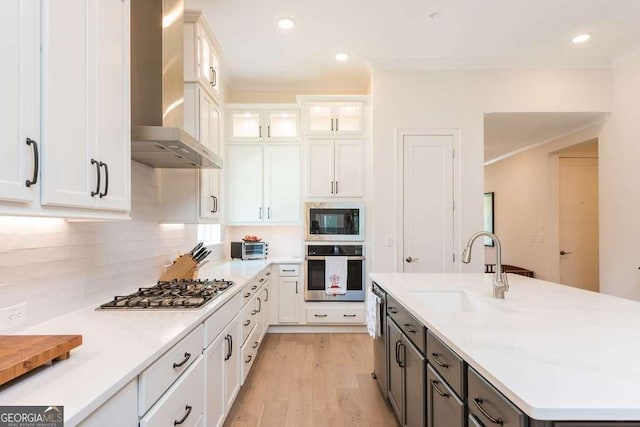 kitchen featuring stainless steel appliances, sink, white cabinets, tasteful backsplash, and wall chimney range hood