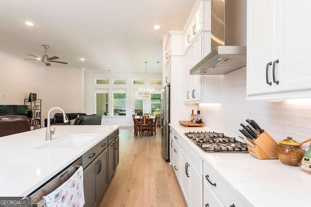 kitchen with wall chimney exhaust hood, decorative light fixtures, stainless steel appliances, white cabinets, and sink