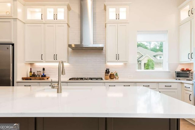 kitchen with stainless steel refrigerator, an island with sink, wall chimney exhaust hood, white cabinetry, and gas cooktop