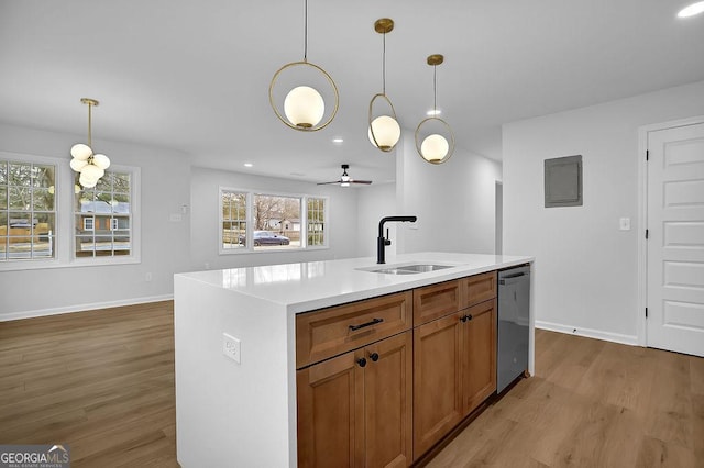 kitchen featuring brown cabinetry, an island with sink, light countertops, stainless steel dishwasher, and a sink