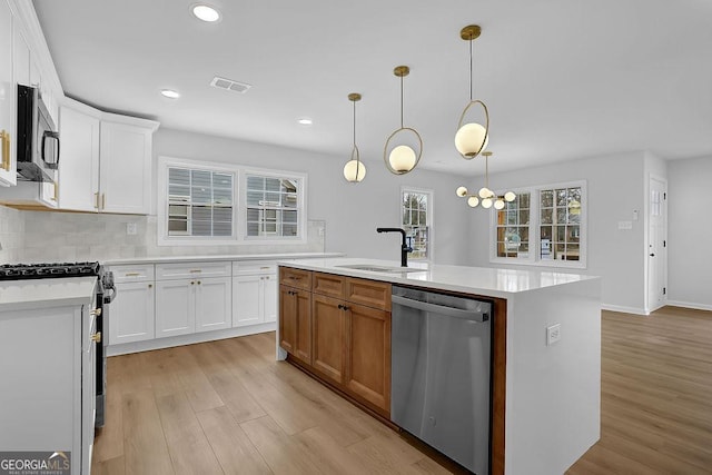 kitchen featuring stainless steel appliances, light countertops, a kitchen island with sink, and white cabinets