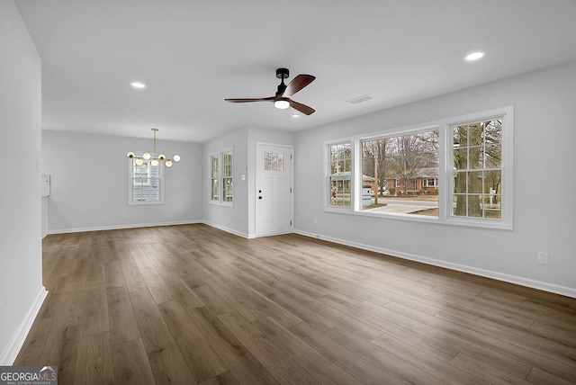 unfurnished living room with recessed lighting, ceiling fan with notable chandelier, wood finished floors, visible vents, and baseboards