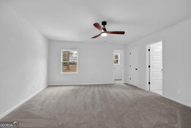 empty room with baseboards, a ceiling fan, and light colored carpet