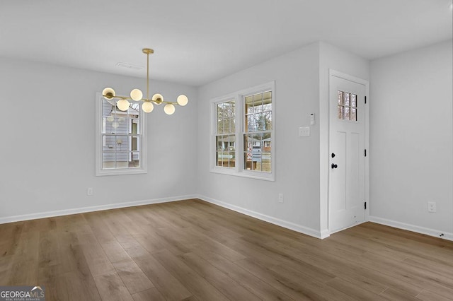 unfurnished dining area with visible vents, baseboards, a chandelier, and wood finished floors