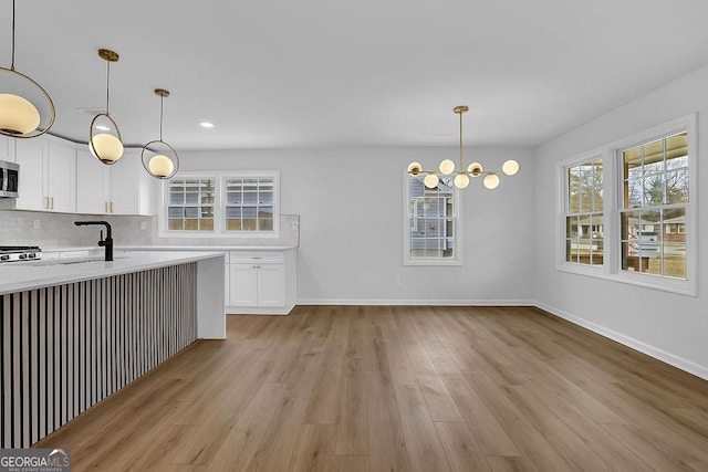 kitchen with white cabinets, decorative backsplash, decorative light fixtures, light countertops, and a sink