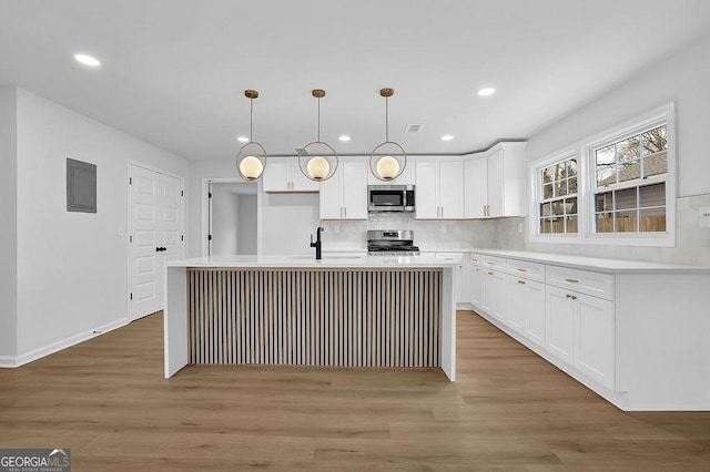 kitchen with a center island with sink, appliances with stainless steel finishes, hanging light fixtures, light countertops, and white cabinetry