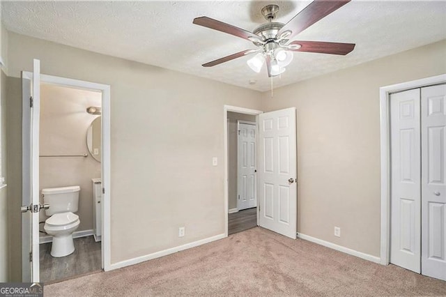 unfurnished bedroom featuring a textured ceiling, a closet, connected bathroom, light colored carpet, and ceiling fan