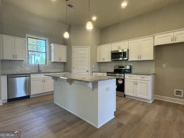 kitchen featuring light stone counters, hanging light fixtures, stainless steel appliances, a kitchen island, and white cabinetry