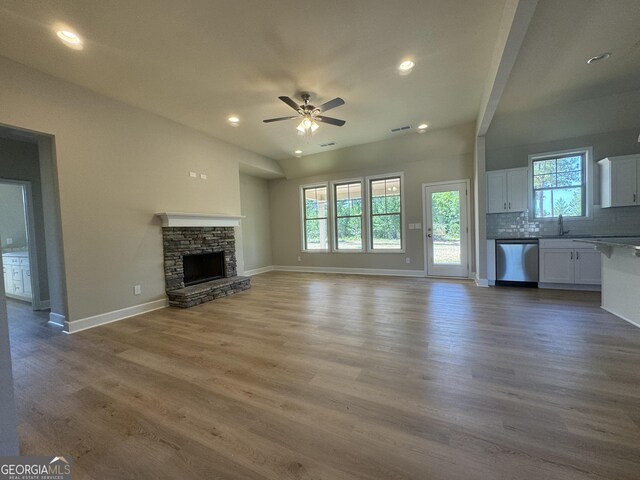 unfurnished living room featuring ceiling fan, a stone fireplace, sink, and hardwood / wood-style flooring