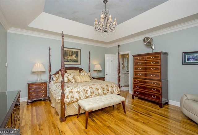 bedroom with light hardwood / wood-style flooring, ensuite bath, a chandelier, a tray ceiling, and crown molding