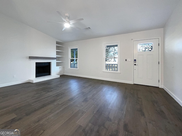 unfurnished living room featuring ceiling fan, built in shelves, a fireplace, and dark hardwood / wood-style floors