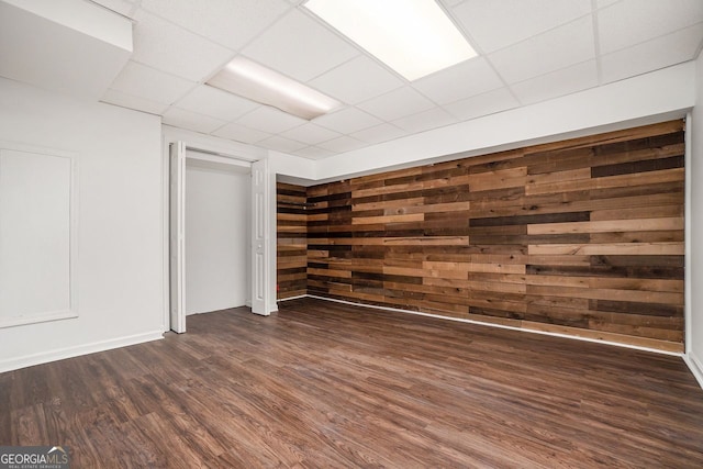 interior space with dark hardwood / wood-style floors, a paneled ceiling, and wood walls