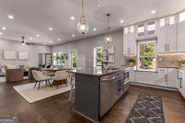 kitchen featuring stainless steel appliances, white cabinetry, dark stone countertops, and a kitchen island with sink