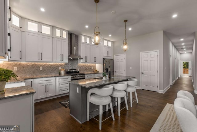 kitchen with white cabinets, stainless steel appliances, wall chimney range hood, and a kitchen island with sink