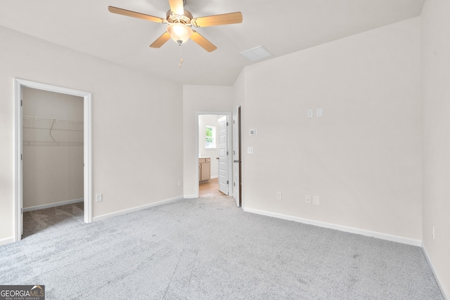 unfurnished bedroom with a walk in closet, a closet, ceiling fan, and light colored carpet