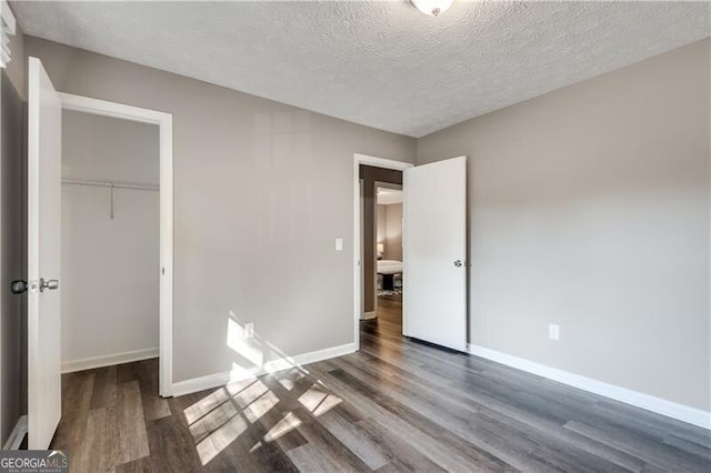 unfurnished bedroom featuring a textured ceiling, dark hardwood / wood-style flooring, a spacious closet, and a closet