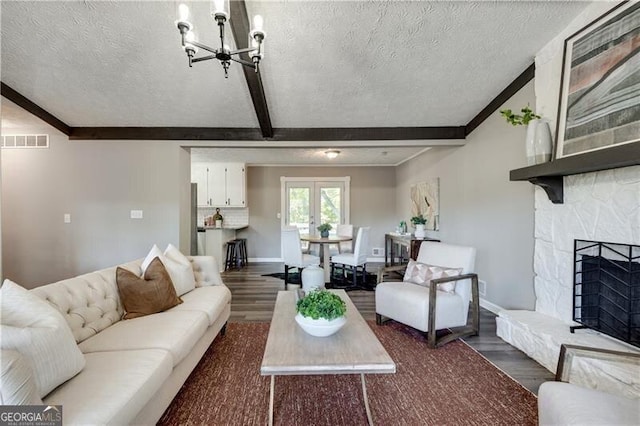 living room with a fireplace, a textured ceiling, beamed ceiling, dark hardwood / wood-style flooring, and a chandelier