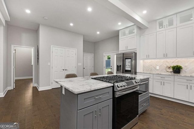 kitchen with light stone counters, decorative backsplash, a kitchen island, white cabinets, and appliances with stainless steel finishes