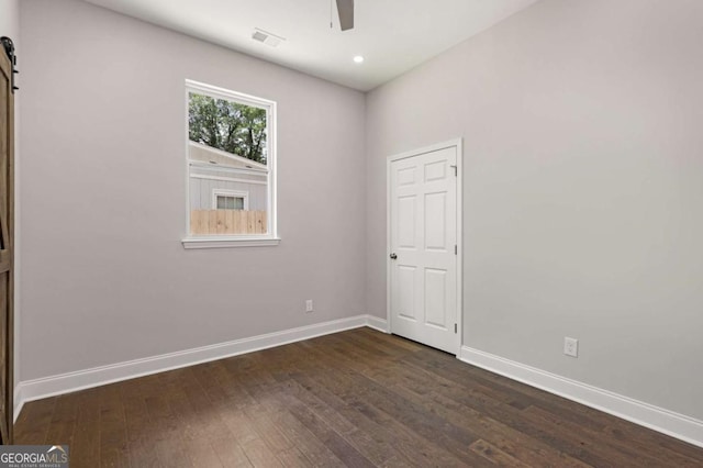 empty room featuring ceiling fan, a barn door, and dark hardwood / wood-style floors