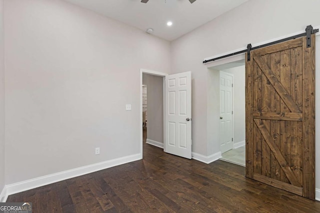 unfurnished room featuring ceiling fan, a barn door, and dark hardwood / wood-style floors