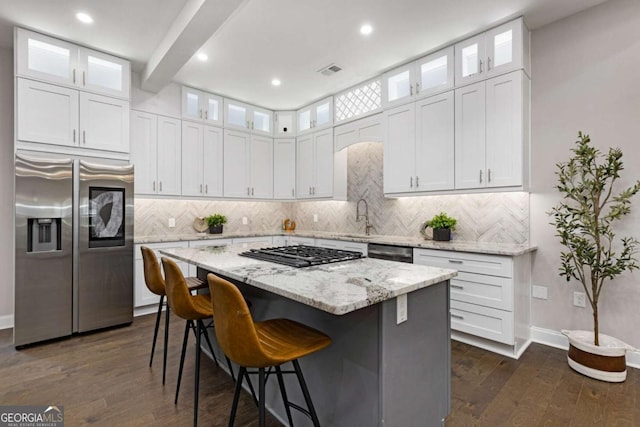 kitchen with white cabinetry, beamed ceiling, light stone counters, a kitchen island, and appliances with stainless steel finishes