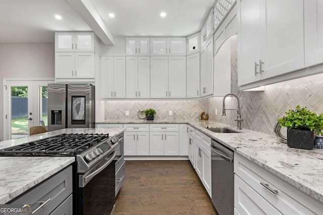 kitchen with sink, appliances with stainless steel finishes, white cabinets, light stone counters, and dark wood-type flooring