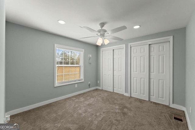 unfurnished bedroom with two closets, ceiling fan, and carpet floors