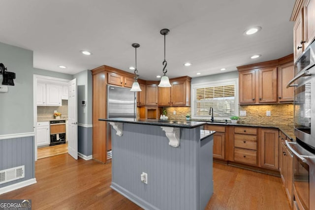 kitchen featuring a kitchen breakfast bar, appliances with stainless steel finishes, light wood-type flooring, a center island, and pendant lighting