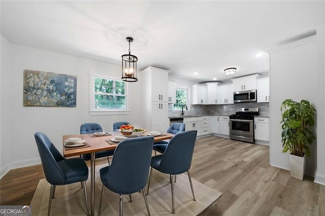 dining space with sink, light wood-type flooring, and an inviting chandelier