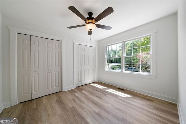 unfurnished bedroom with multiple closets, ceiling fan, and light hardwood / wood-style floors