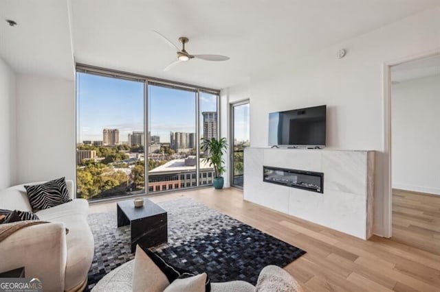 living room with ceiling fan, a wall of windows, and light hardwood / wood-style flooring