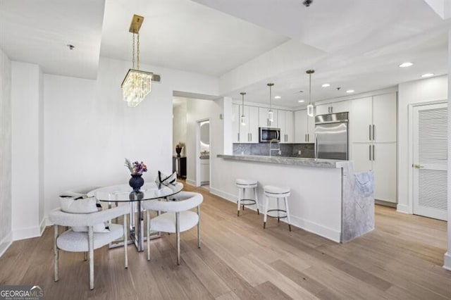 kitchen featuring appliances with stainless steel finishes, pendant lighting, white cabinets, kitchen peninsula, and light stone countertops