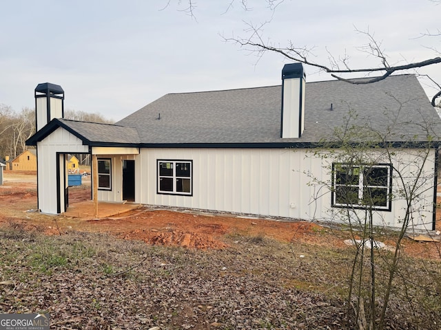 rear view of house with board and batten siding, roof with shingles, and a chimney